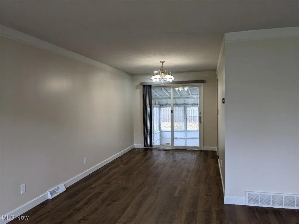 Spare room featuring ornamental molding, a chandelier, and dark wood-style flooring