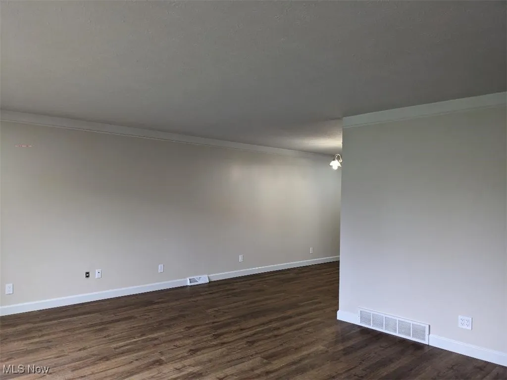 Unfurnished room featuring dark wood-style floors, crown molding, a textured ceiling, and a chandelier