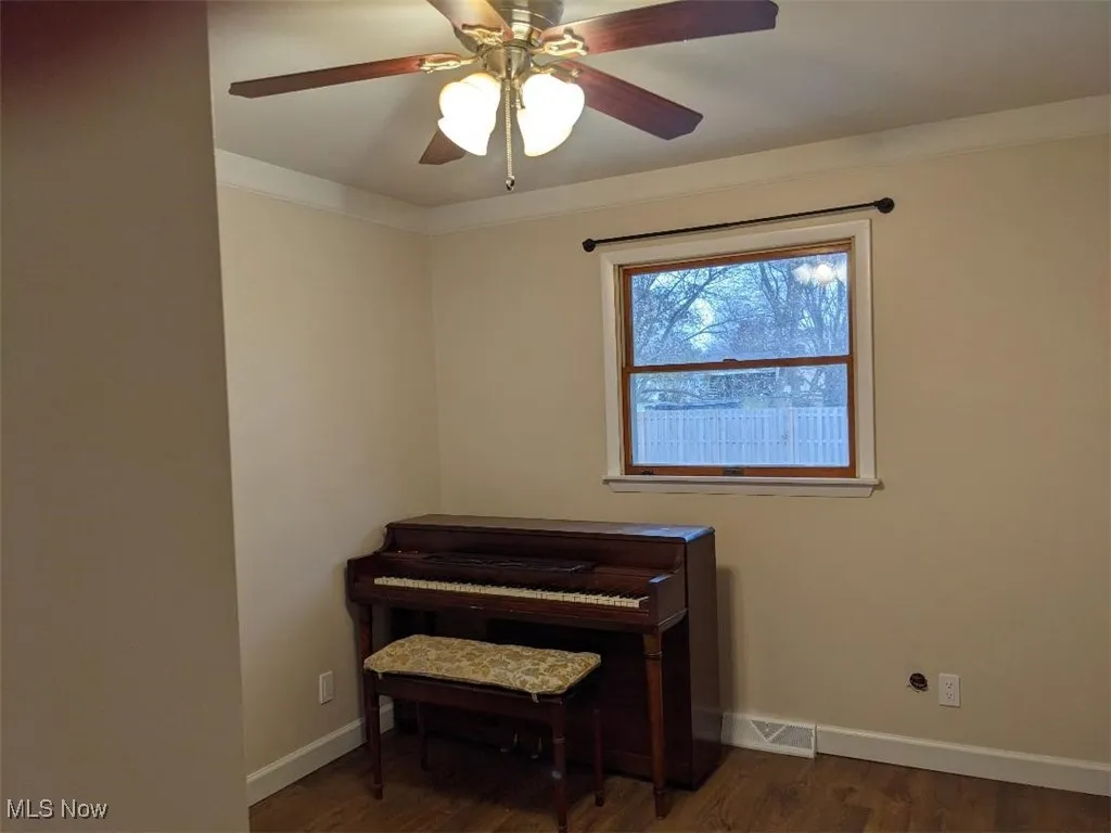 Sitting room featuring dark wood-type flooring, ceiling fan, and crown molding