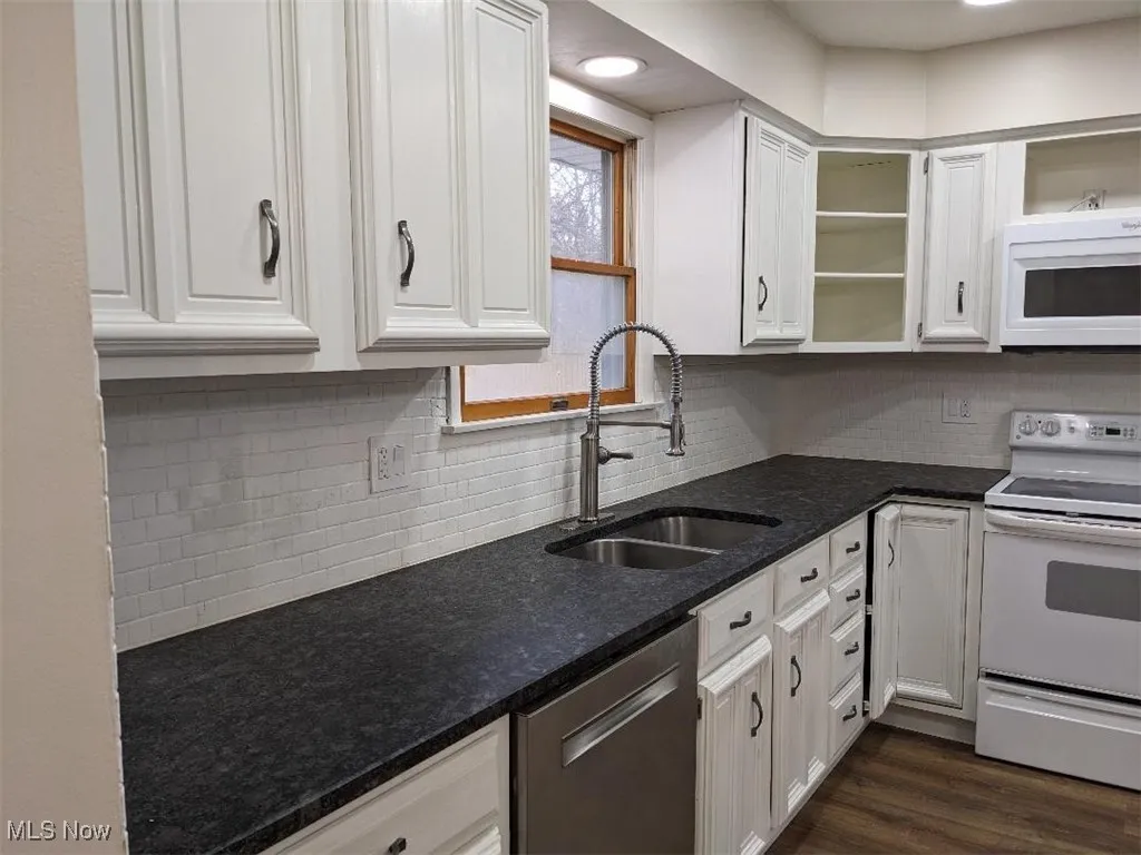 Kitchen with white appliances, dark stone counters, white cabinets, dark wood-style floors, and decorative backsplash