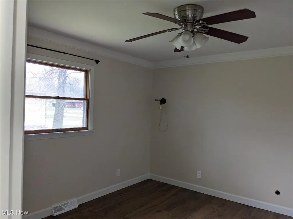 Unfurnished room with ornamental molding, ceiling fan, and dark wood-style floors