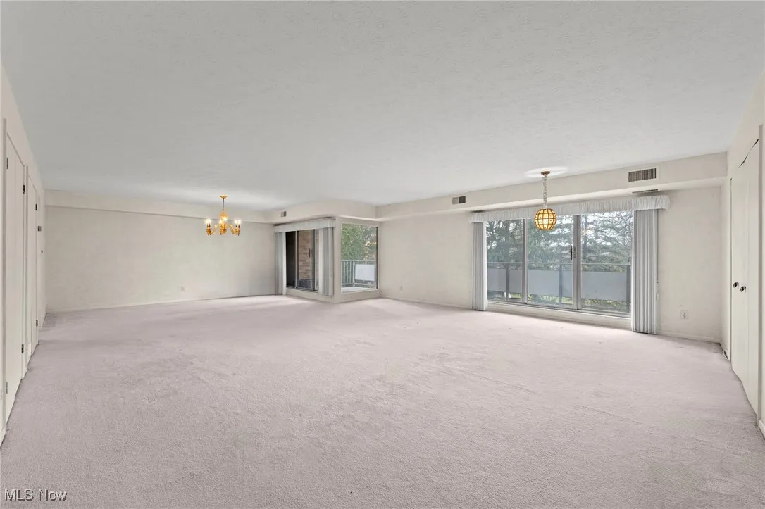 Open, spacious living/dining room area with balcony, chandelier and carpet
