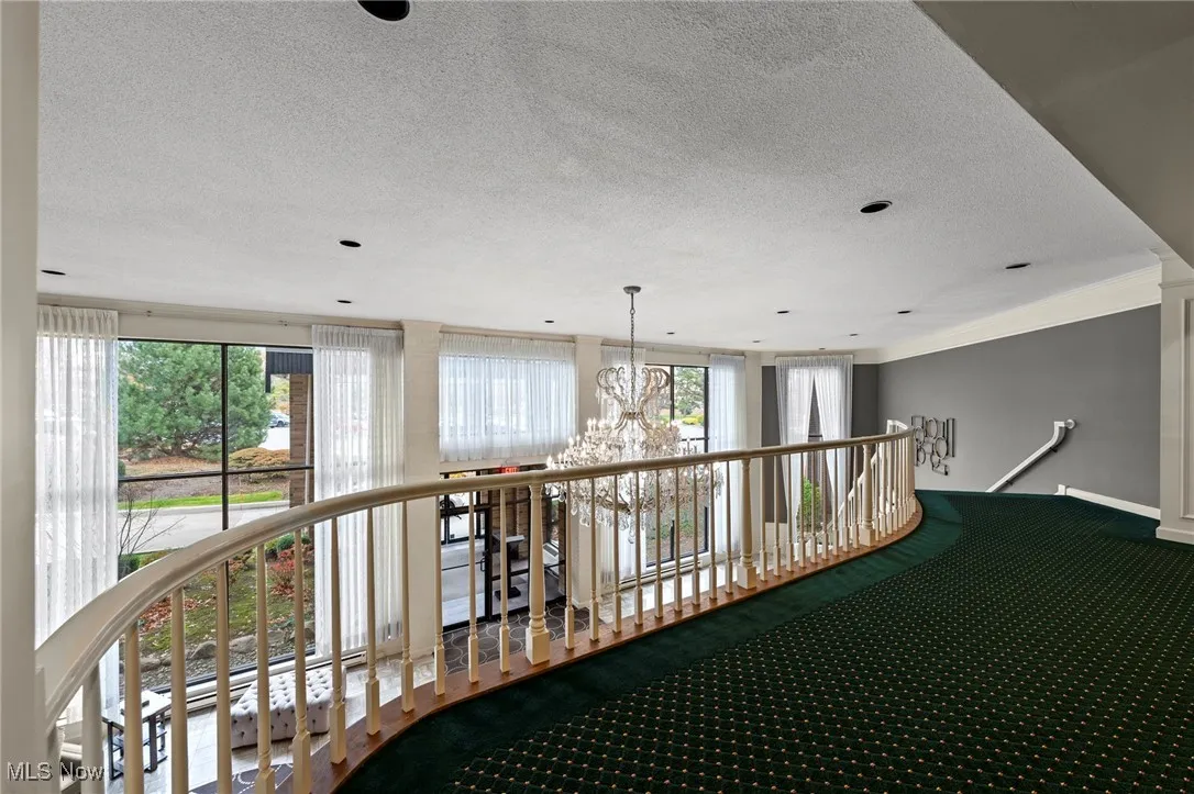 Hallway featuring a chandelier, a textured ceiling, carpet, crown molding, and an upstairs landing