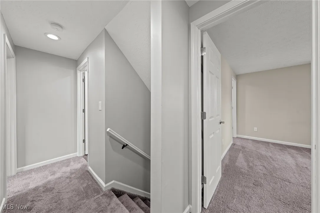 Hall featuring an upstairs landing, carpet flooring, and a textured ceiling