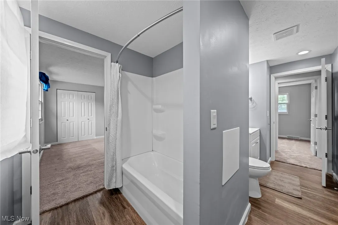 Full bathroom with a textured ceiling, shower / bath combo, wood finished floors, and vanity