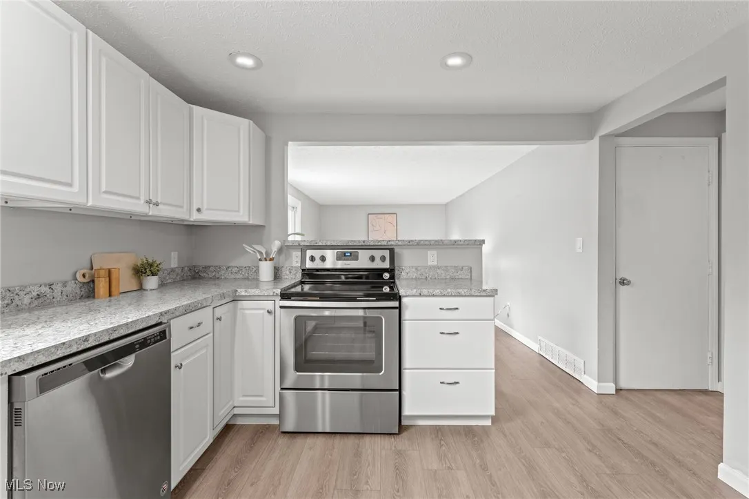 Kitchen with appliances with stainless steel finishes, white cabinetry, light countertops, a peninsula, and a textured ceiling