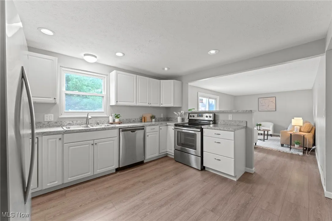 Kitchen with white cabinetry, appliances with stainless steel finishes, open floor plan, light wood-type flooring, and a peninsula