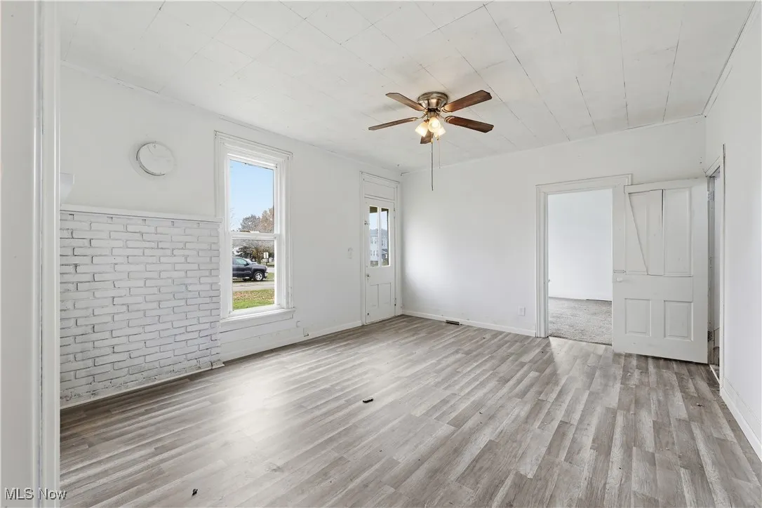 Empty room featuring brick wall, a ceiling fan, and light wood-style flooring