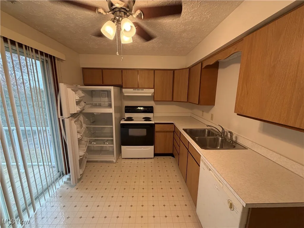 Kitchen featuring light countertops, white appliances, light floors, a ceiling fan, and a textured ceiling