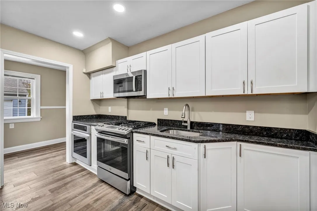 Kitchen featuring appliances with stainless steel finishes, white cabinets, dark stone counters, light wood-type flooring, and recessed lighting