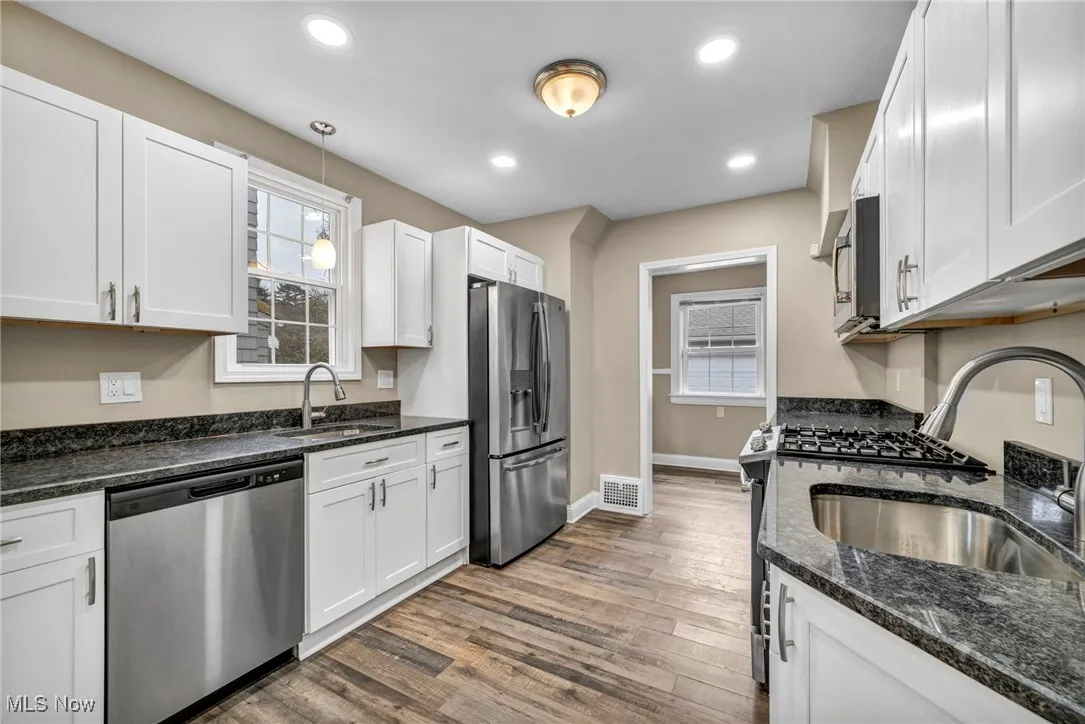 Kitchen featuring dark stone counters, appliances with stainless steel finishes, dark wood finished floors, decorative light fixtures, and white cabinets