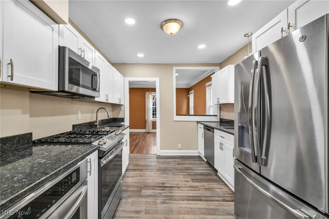 Kitchen with stainless steel appliances, dark wood-style flooring, white cabinetry, dark stone counters, and recessed lighting