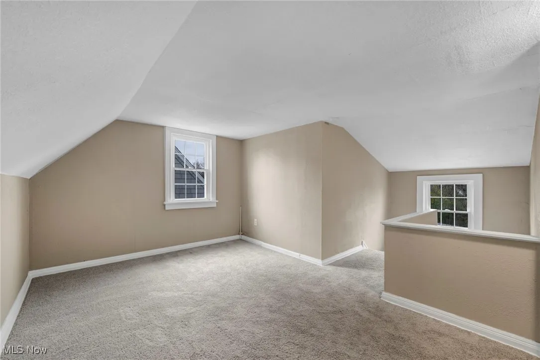 Bonus room with lofted ceiling, healthy amount of natural light, light colored carpet, and a textured ceiling