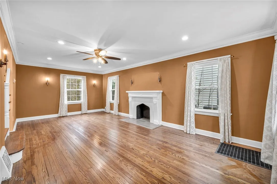 Unfurnished living room featuring ornamental molding, light wood-style flooring, a fireplace with flush hearth, ceiling fan, and recessed lighting