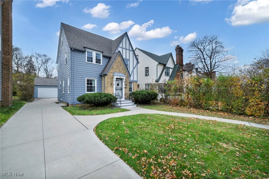 Tudor house featuring an outbuilding, a front lawn, roof with shingles, a garage, and stone siding
