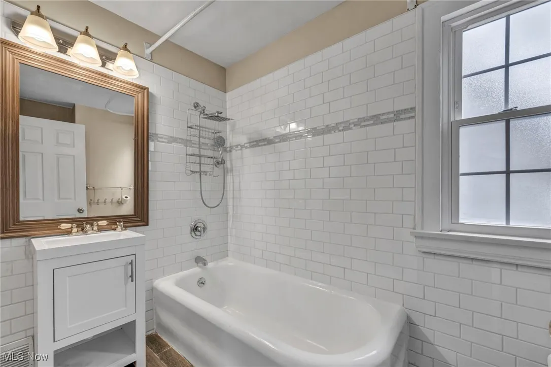 Full bath with tile walls, shower / tub combination, plenty of natural light, and vanity