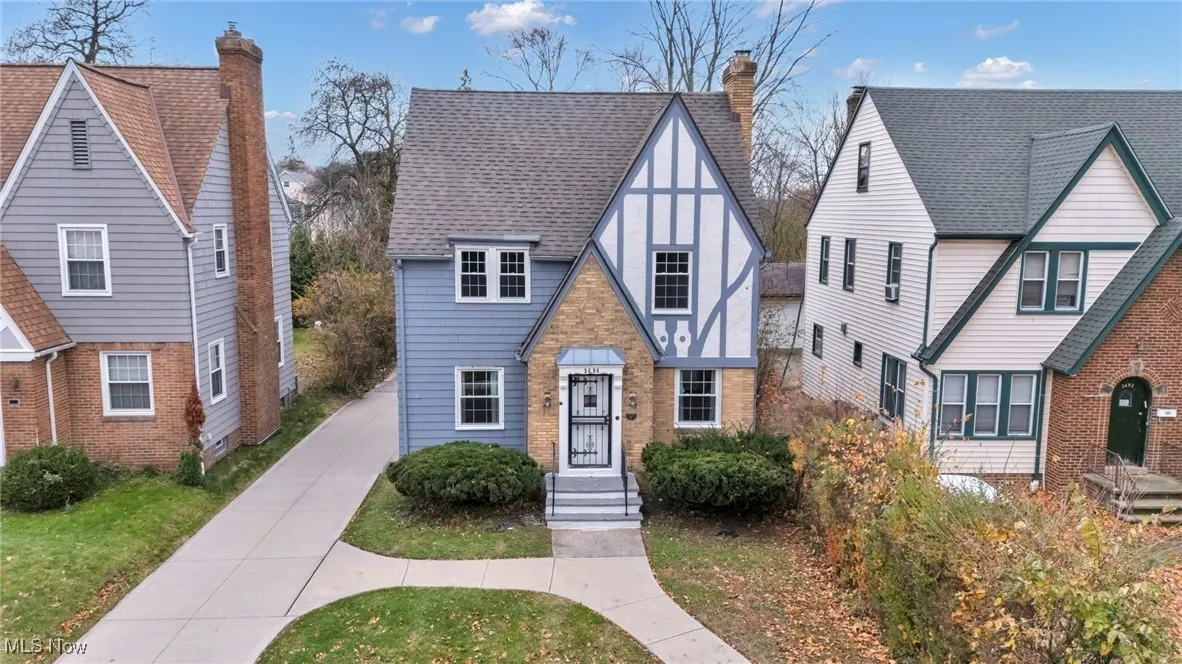 Tudor-style house featuring a chimney, a shingled roof, and a front yard