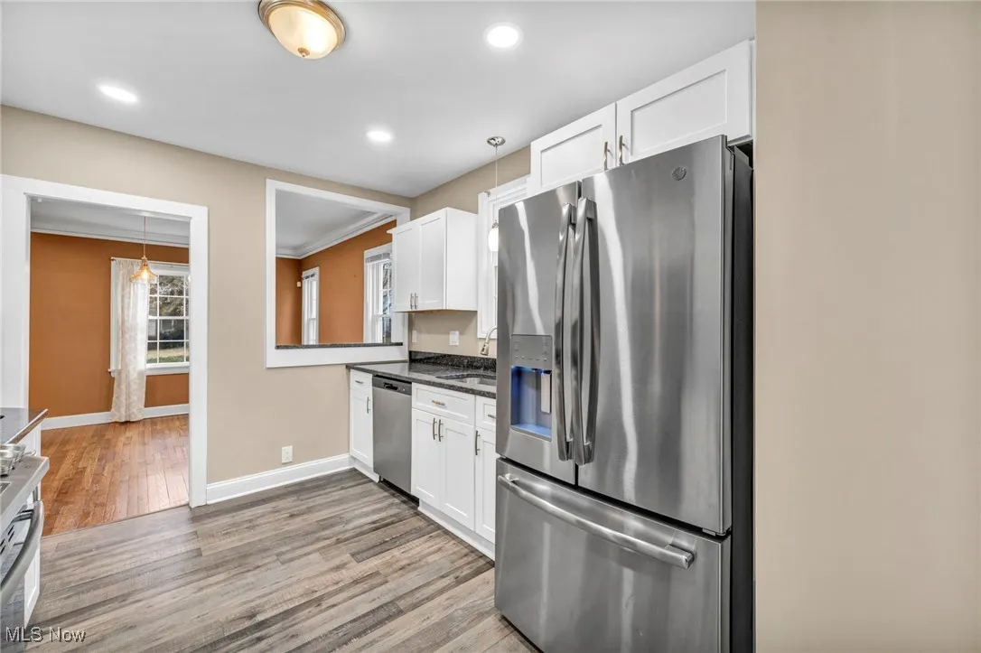 Kitchen featuring appliances with stainless steel finishes, pendant lighting, white cabinetry, light wood-type flooring, and crown molding