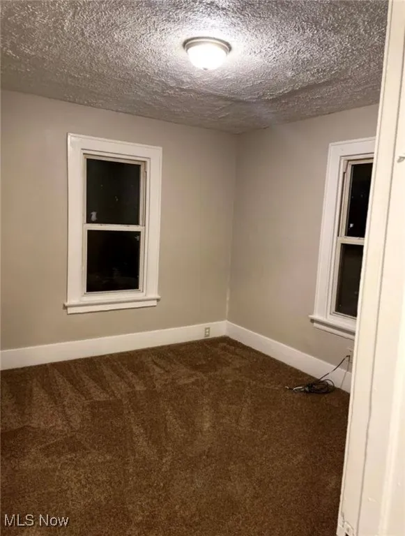 Unfurnished room with a textured ceiling and dark colored carpet