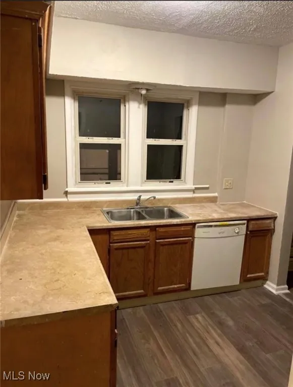 Kitchen with light countertops, a textured ceiling, dishwasher, dark wood-style flooring, and brown cabinets