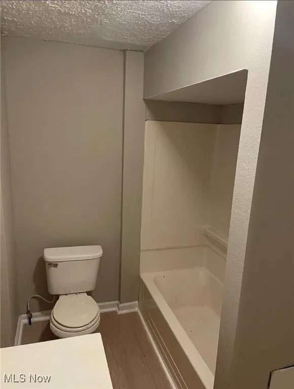 Full bathroom with a textured ceiling and wood finished floors