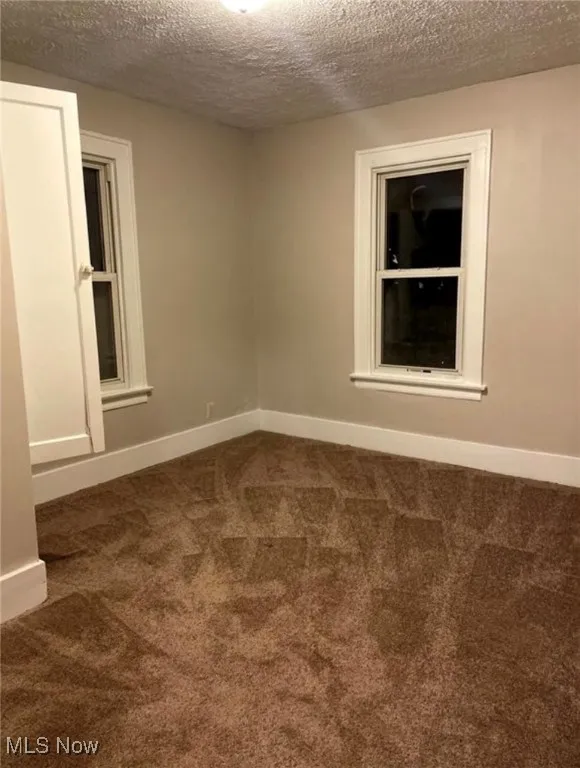 Empty room with a textured ceiling and dark carpet