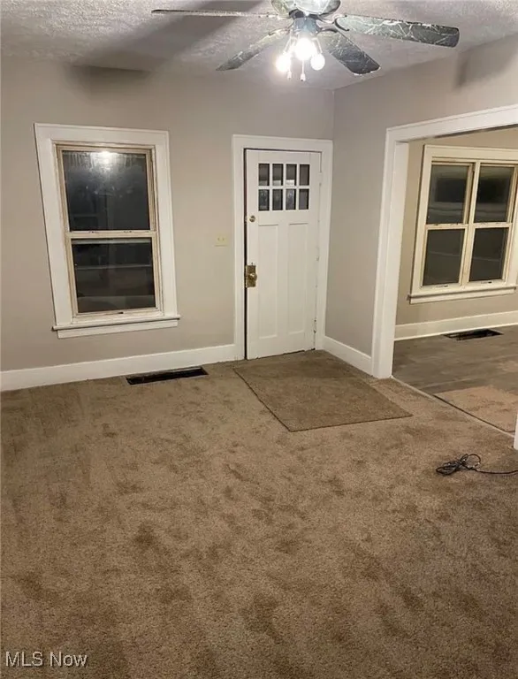 Carpeted entrance foyer with a textured ceiling and a ceiling fan