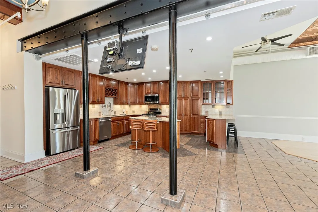 Kitchen featuring a breakfast bar area, decorative backsplash, appliances with stainless steel finishes, brown cabinets, and recessed lighting