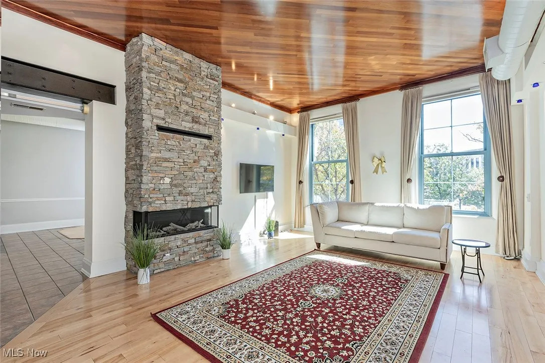 Living room featuring a stone fireplace, wood ceiling, and light wood finished floors