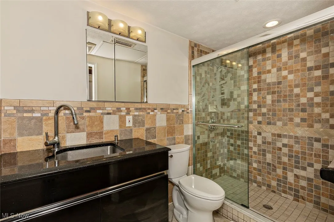 Full bath with a stall shower, vanity, and tile walls
