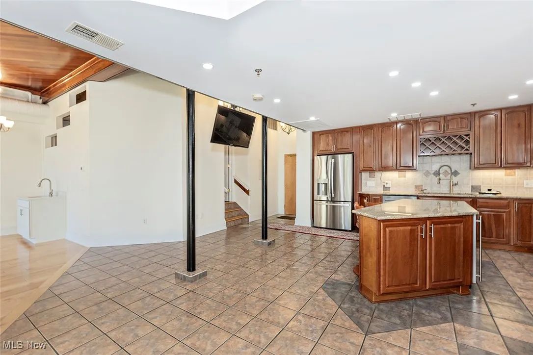 Kitchen featuring brown cabinets, decorative backsplash, light stone countertops, recessed lighting, and stainless steel fridge with ice dispenser