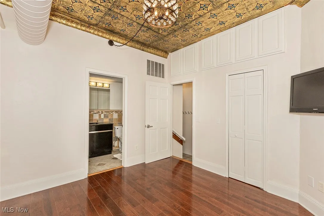 Unfurnished bedroom with an ornate ceiling, dark wood finished floors, a closet, ensuite bathroom, and a chandelier