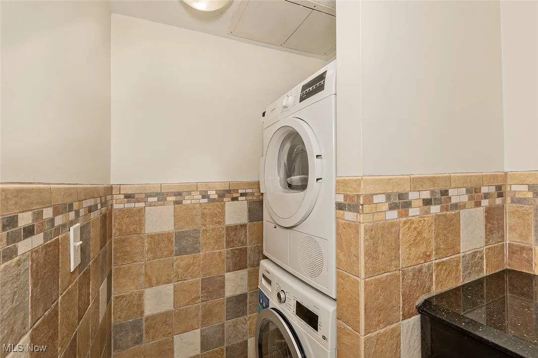 Laundry area featuring stacked washing machine and dryer, tile walls, and a wainscoted wall