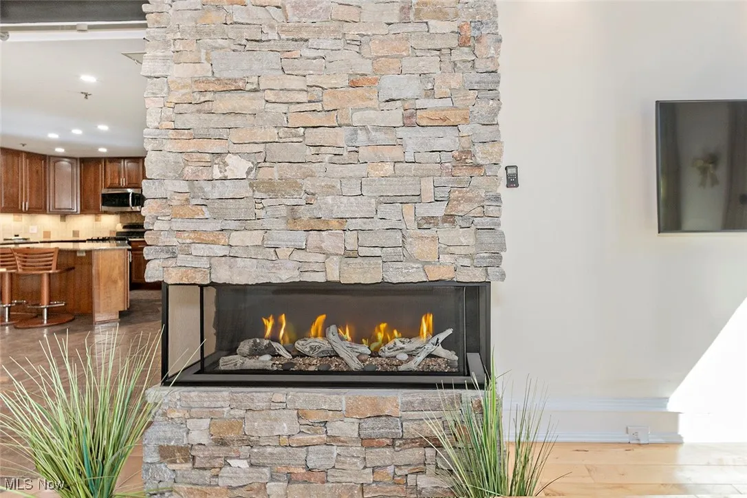 Detailed view of a stone fireplace, wood finished floors, stainless steel microwave, tasteful backsplash, and recessed lighting