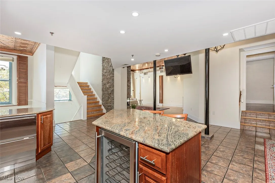 Kitchen featuring light stone counters, wine cooler, a kitchen island, brown cabinetry, and recessed lighting