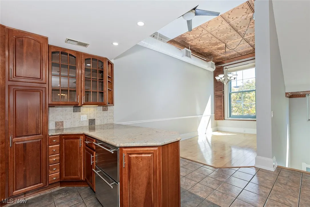 Kitchen with light stone counters, glass insert cabinets, an ornate ceiling, decorative backsplash, and dark tile patterned floors