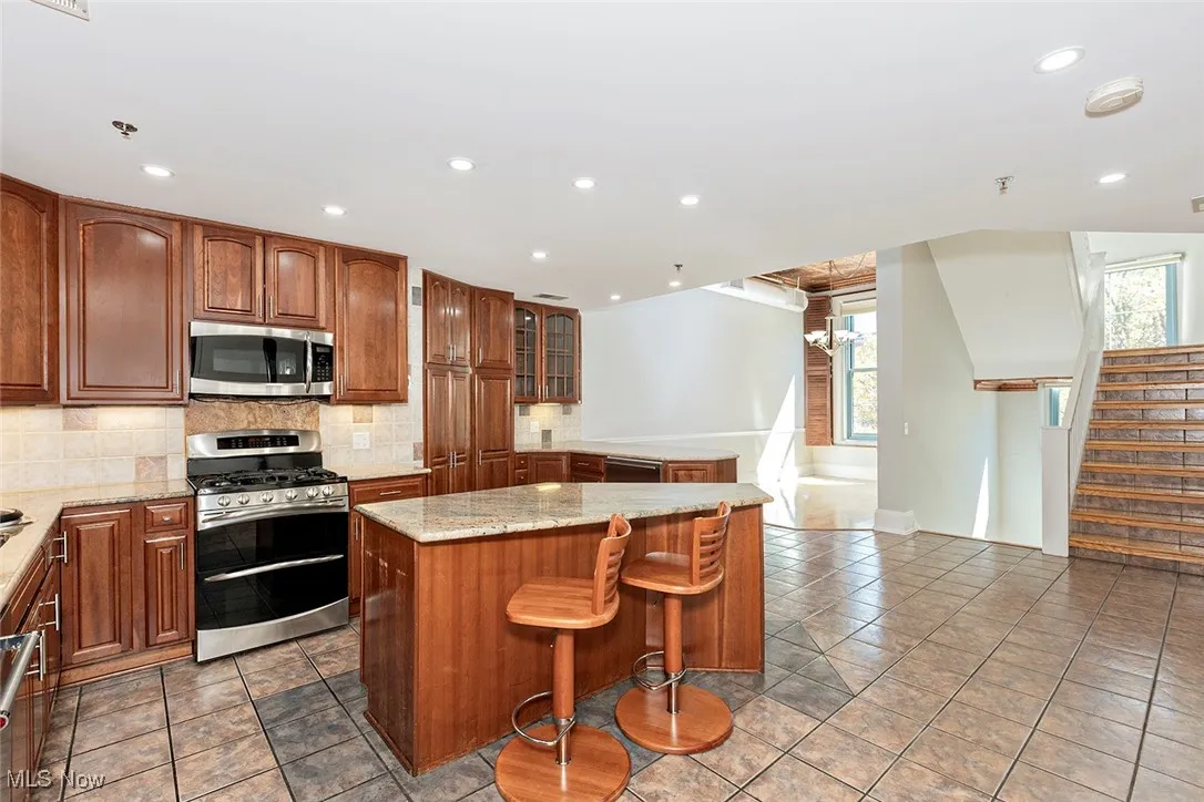 Kitchen with appliances with stainless steel finishes, a center island, backsplash, a chandelier, and a breakfast bar