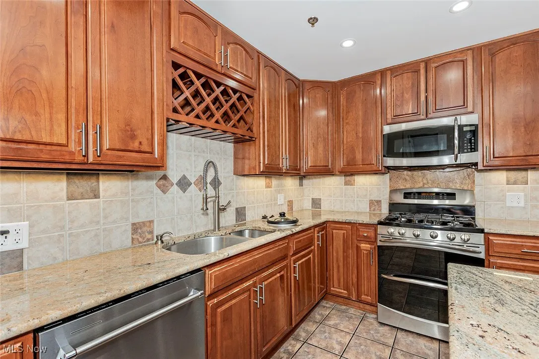 Kitchen featuring appliances with stainless steel finishes, light stone countertops, brown cabinets, tasteful backsplash, and light tile patterned flooring