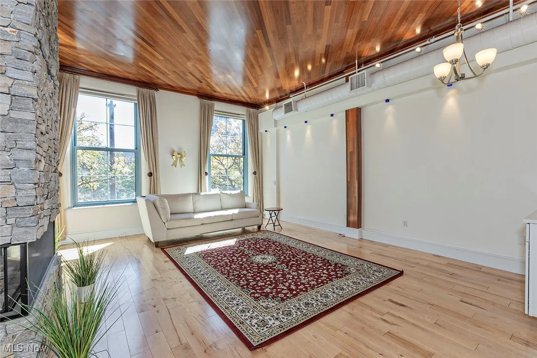 Living room featuring light wood-style floors, a stone fireplace, wooden ceiling, and a chandelier