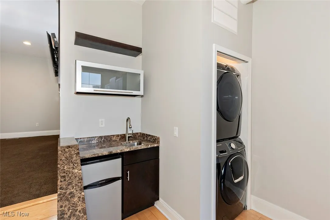 Washroom with stacked washer / dryer and light wood-style floors
