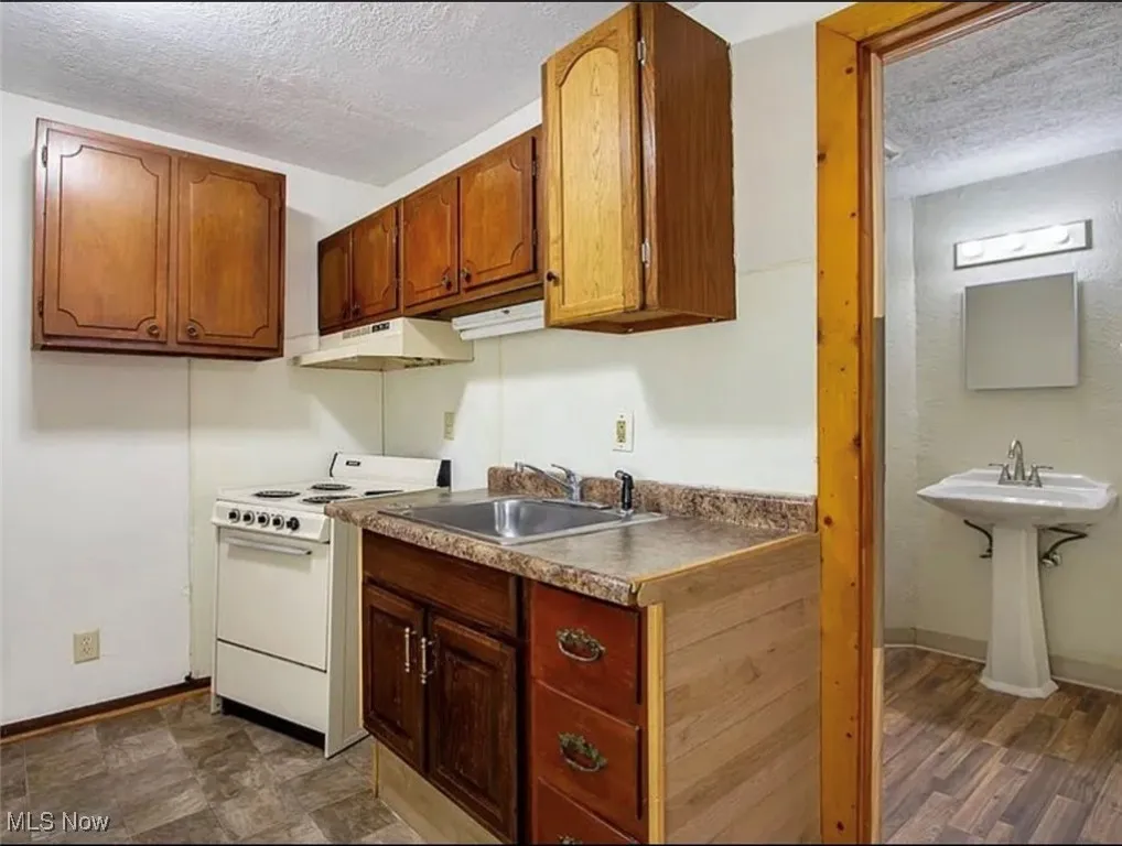 Kitchen with a textured ceiling, white electric range oven, under cabinet range hood, and brown cabinetry