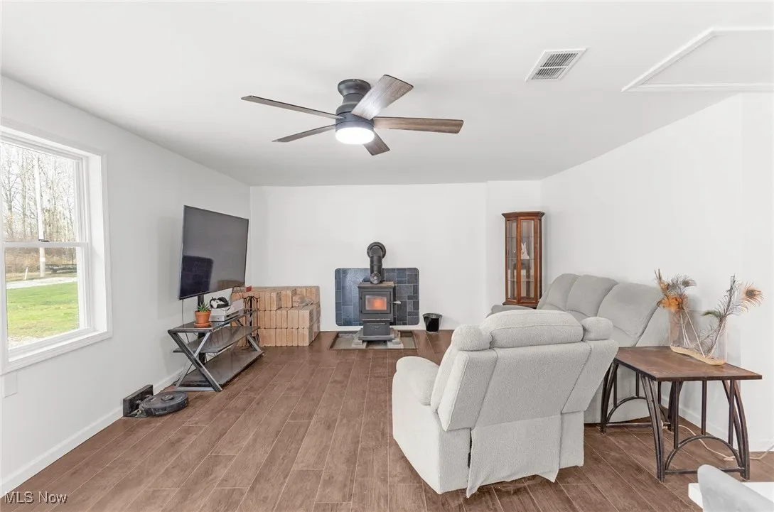 Living area featuring a wood stove, wood finished floors, and ceiling fan