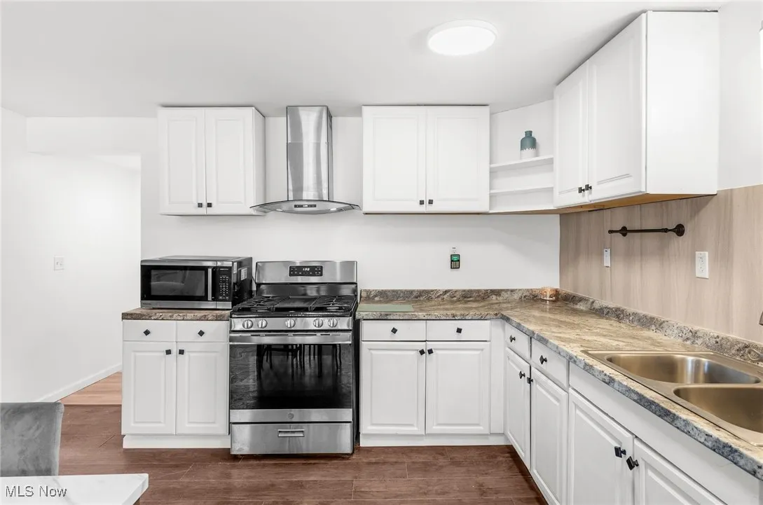 Kitchen with stainless steel appliances, wall chimney exhaust hood, open shelves, white cabinets, and dark wood-style flooring