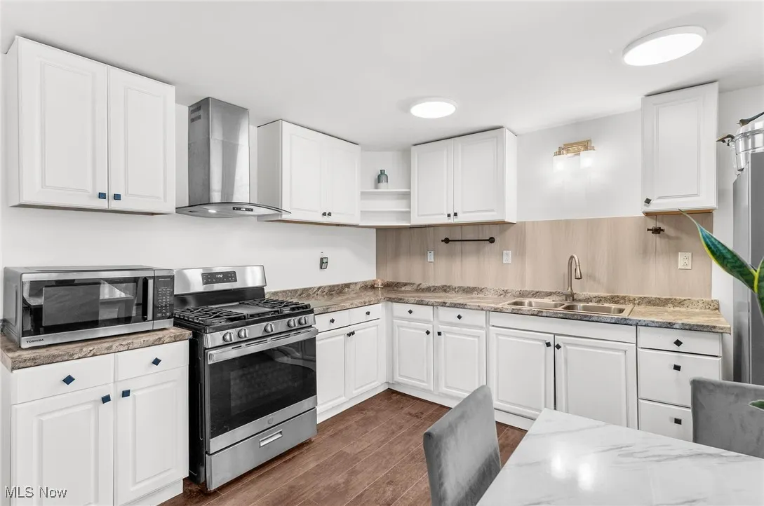 Kitchen featuring stainless steel appliances, wall chimney exhaust hood, white cabinetry, open shelves, and dark wood-style flooring