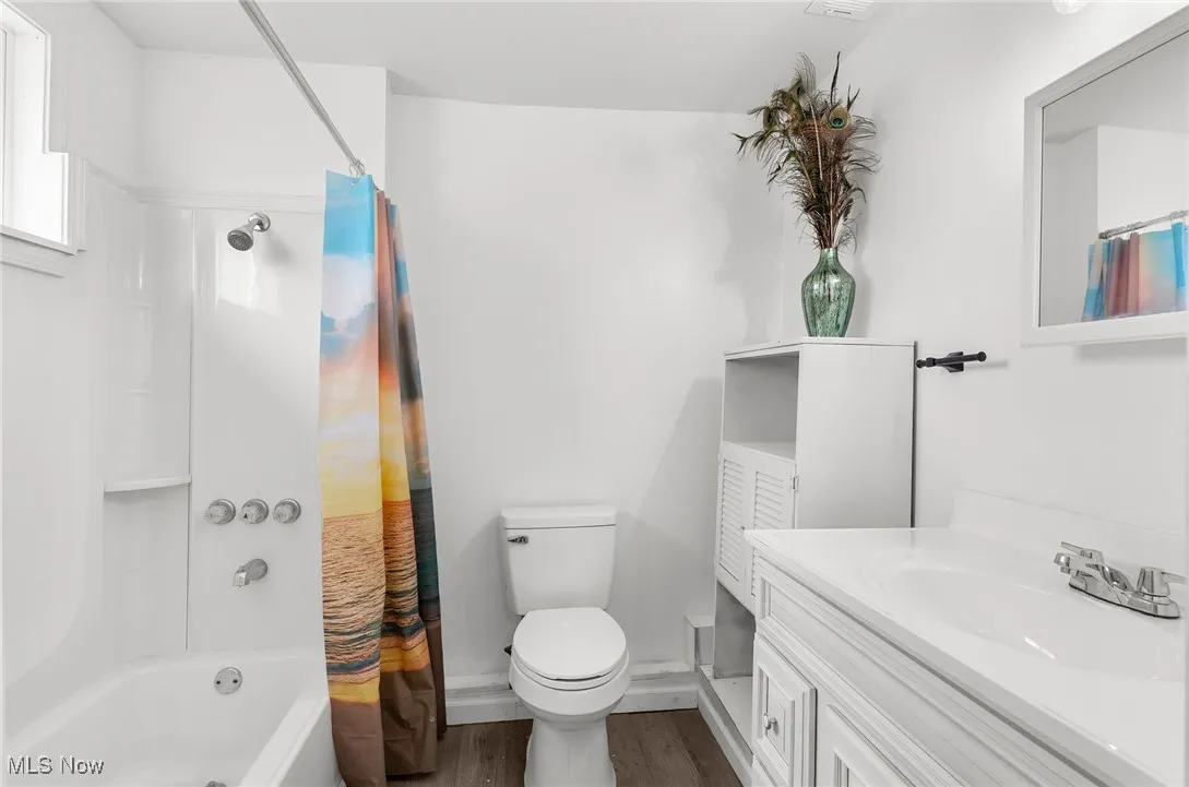 Full bath featuring shower / bath combo with shower curtain, vanity, and dark wood finished floors