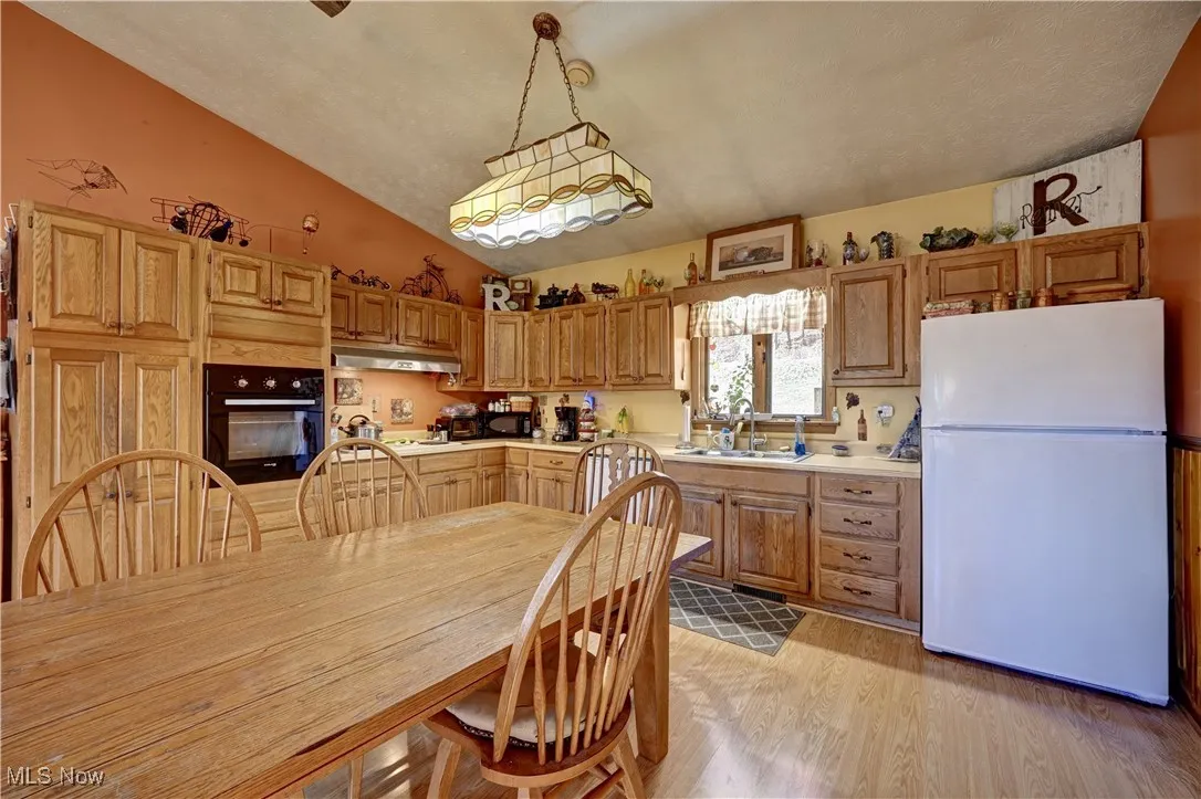 Kitchen with freestanding refrigerator, light countertops, oven, vaulted ceiling, and hanging light fixtures