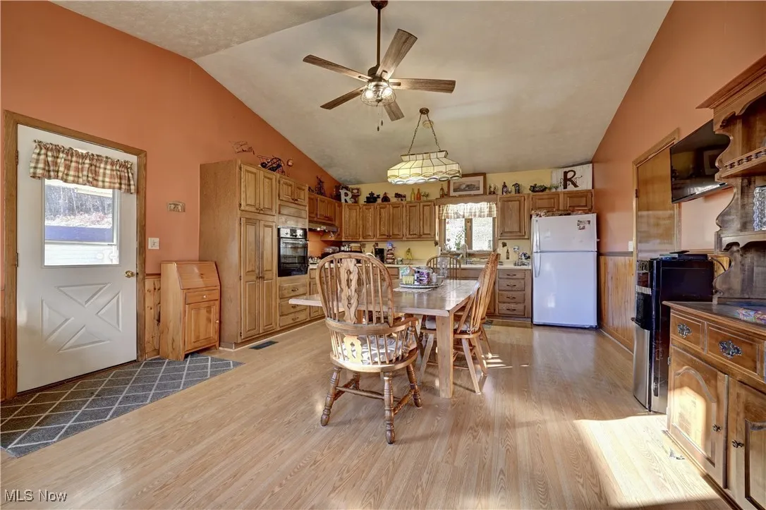 Dining area featuring light wood finished floors, a ceiling fan, lofted ceiling, and wainscoting