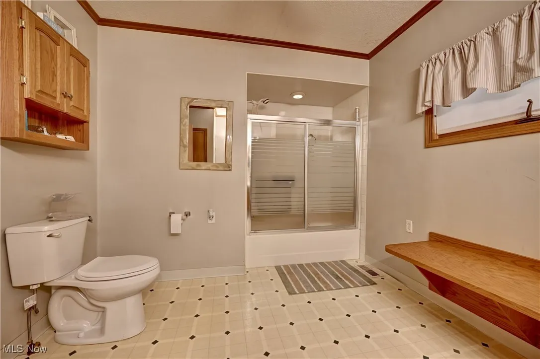 Bathroom featuring combined bath / shower with glass door, ornamental molding, and light flooring