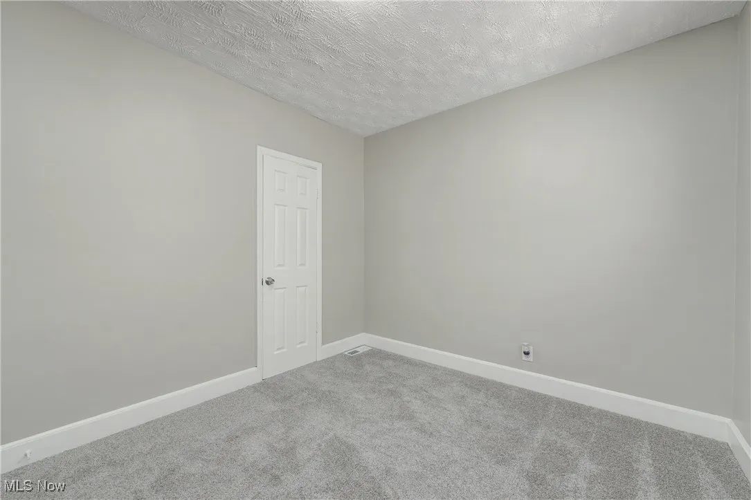 Carpeted empty room featuring a textured ceiling and baseboards