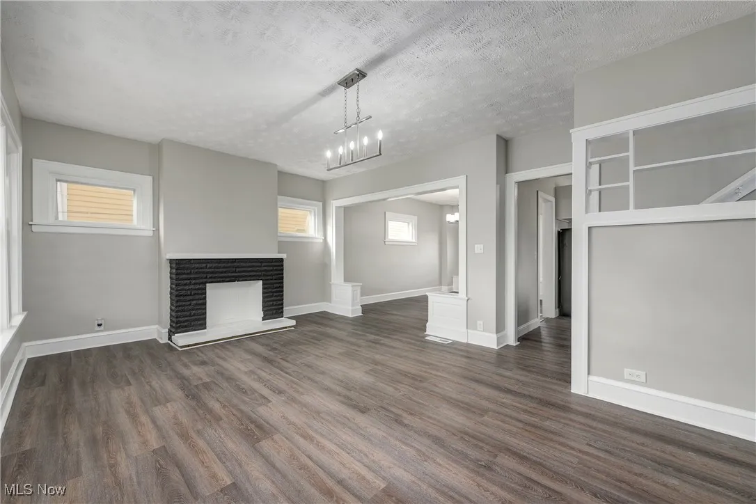 Unfurnished living room with a fireplace, dark wood-style flooring, a textured ceiling, and a chandelier